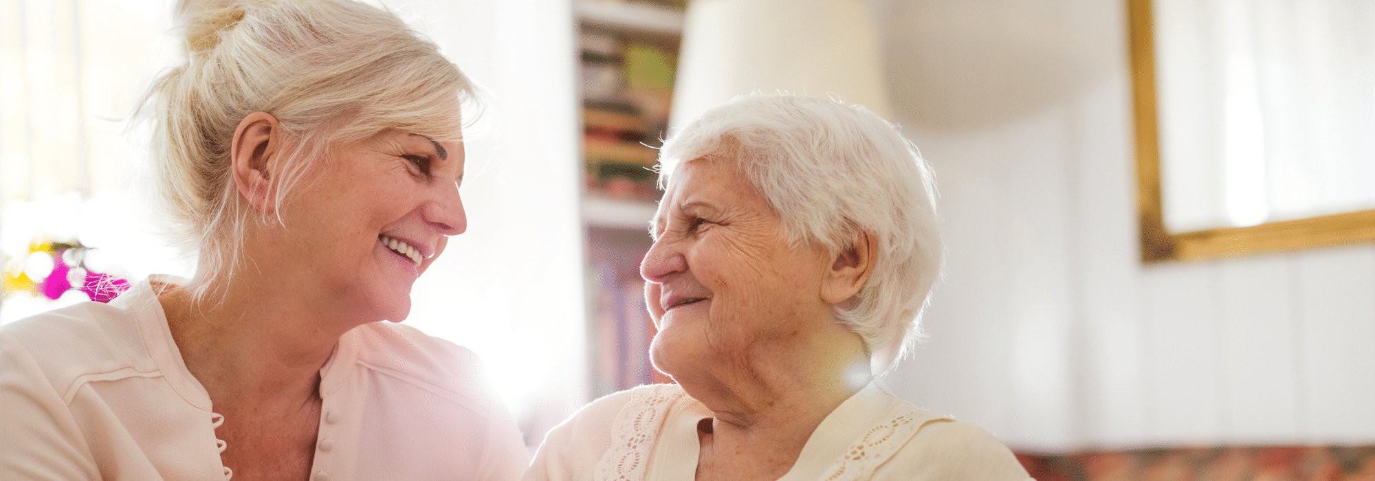 two elderly ladies smiling to each other as the drink tea together