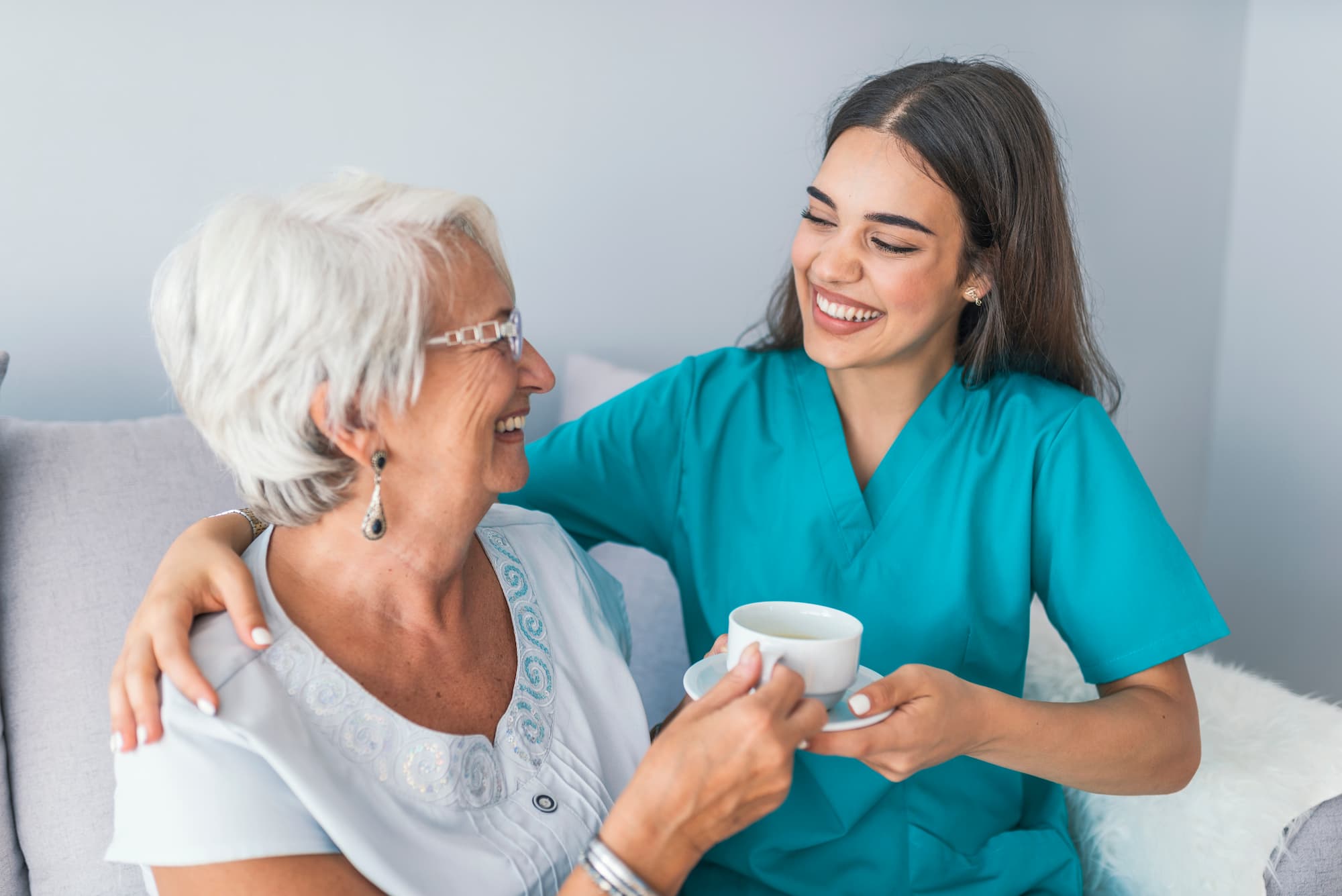 Happy senior woman chatting with her nurse as the nurse hands her a cup