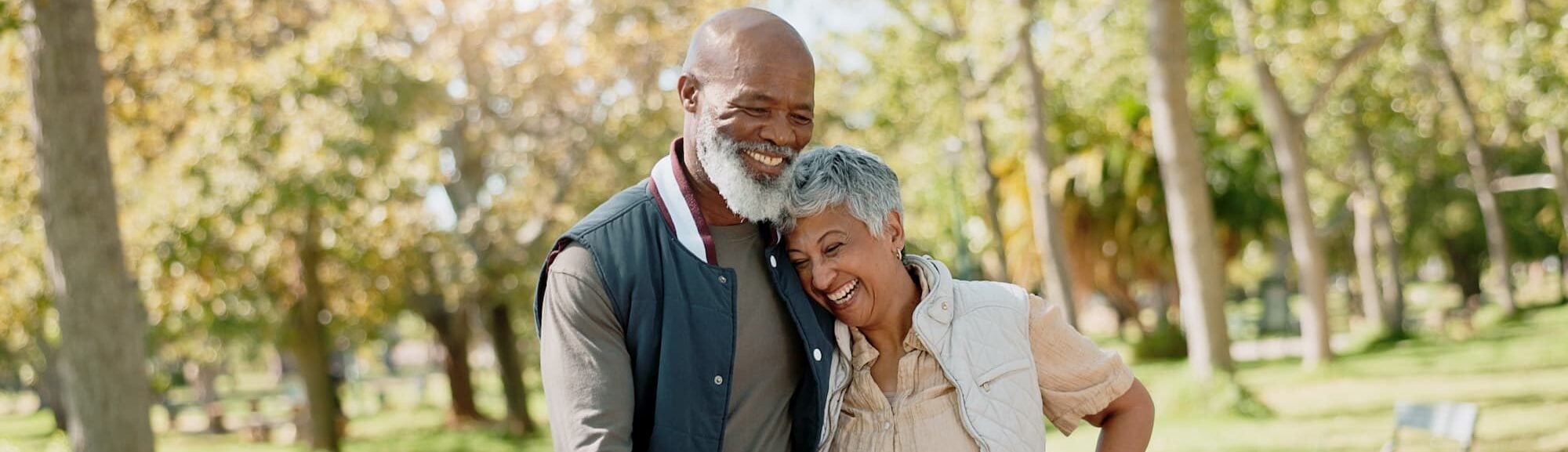 a senior couple goes for a walk on a paved trail through a wooded park