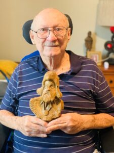 A portrait of Jerry holding a whittled mountain man figurine